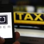 File illustration picture showing the logo of car-sharing service app Uber on a smartphone next to the picture of an official German taxi sign