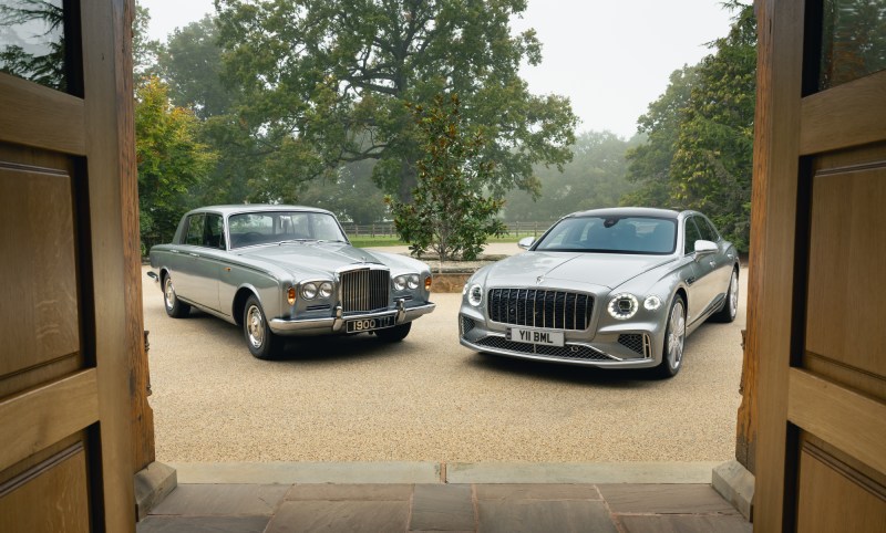 Bentley 1965 T Series and 2025 Flying Spur Azure at speed through an open doorway parked on a gravel driveway.